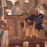 Elderly architect examining wooden city skyline model